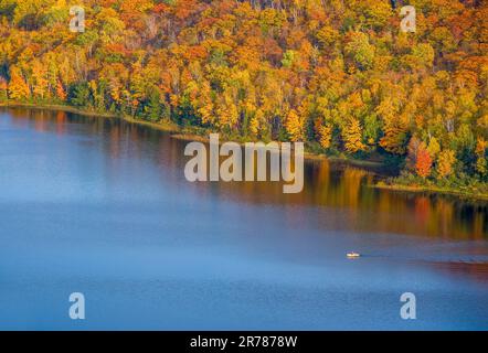 Auf der oberen Halbinsel von Michigan, der Herbstfarben rund um den See, zieht ein einsamer Bootsfahrer über den Wolkensee. Stockfoto