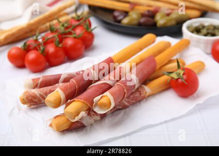 Köstliche Grissini-Sticks mit Prosciutto und Snacks auf weißem Tisch, Nahaufnahme Stockfoto