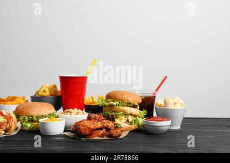 Pommes Frites, Burger und andere Fast Food auf einem Holztisch vor weißem Hintergrund Stockfoto