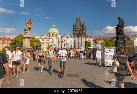 PRAG, TSCHECHISCHE REPUBLIK - Touristen, die die Karlsbrücke überqueren, Mann auf Roller. Der Old Town Bridge Tower befindet sich hinter dem Gebäude. Stockfoto