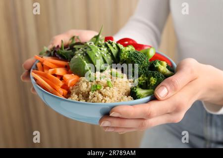 Eine Frau, die eine vegane Schüssel mit Avocados, Karotten und Brokkoli im Haus hält Stockfoto