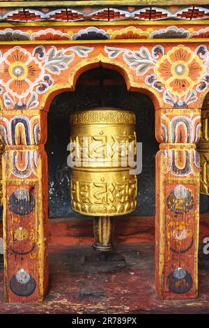 Farbenfrohes vergoldetes Gebetsrad in einer traditionellen bogenförmigen Holznische in Bhutan. Jede Drehung des Rads bringt ein weiteres Gebet in die Welt. Stockfoto