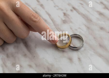 Person Hand nimmt Verlobungsringe im Studio, wunderschöner Schmuck mit Marmorstruktur im Hintergrund, Liebe und Feier mit Ehe, Symbol Stockfoto