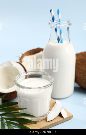 Köstliche vegane Milch, Kokosnüsse und Blätter auf hellblauem Hintergrund Stockfoto