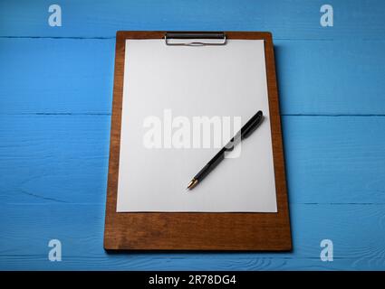 Klemmbrett mit Blatt Papier und Stift auf hellblauem Holztisch. Platz für Text Stockfoto