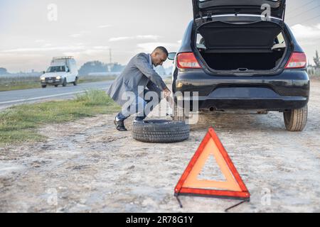 Ein Latino-Mann wechselt einen Platten Reifen am Straßenrand seines Wagens. Stockfoto