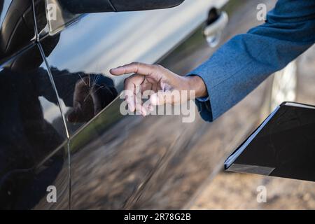 Detail einer Hand eines Versicherungsmaklers, die auf einen Kratzer an einem Auto hinweist. Stockfoto