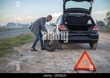 Ein Latino-Mann wechselt einen Platten Reifen am Straßenrand seines Wagens. Stockfoto