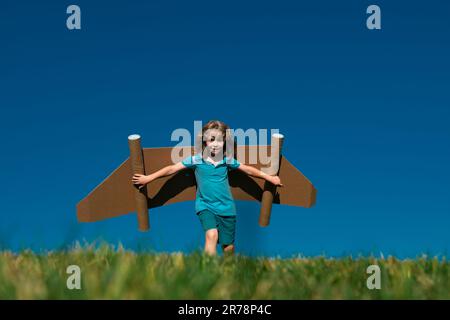 Kind mit Jet Pack Superhelden. Kind Pilot vor Sommerhimmel Hintergrund. Junge mit Papierflugzeug Flug, Spielzeug Flugzeug mit Pappflügeln, Phantasie Stockfoto