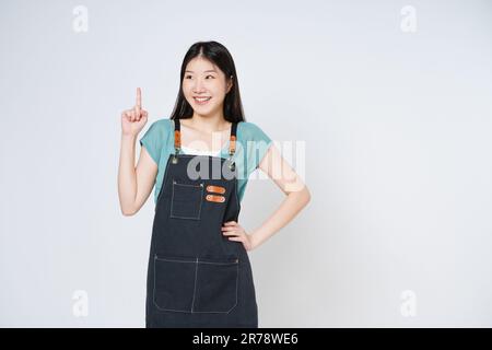 Junge Chefköchin oder Kellnerin blickte nach oben und zeigte auf einen Kopierbereich mit lächelndem Gesicht und glücklich isoliert auf weißem Hintergrund. Stockfoto