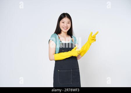 Junge Frau trägt gelbe Gummihandschuhe zum Schutz der Hände und zeigt auf leeren Kopierbereich isoliert auf weißem Hintergrund. Stockfoto