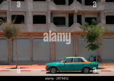 MIRLEFT, Marokko - das alte Mercedes Benz Limousine Grand Taxi parkt vor einem Gebäude mit geschlossenen Stahltüren. Gemeinsames Transportfahrzeug. Stockfoto