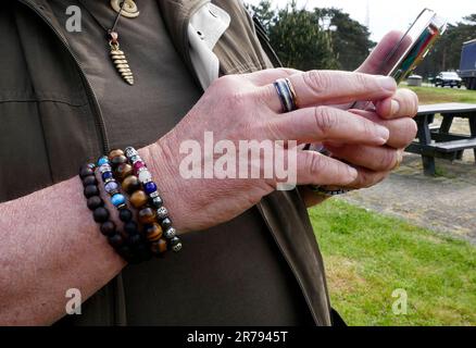 Hände eines modischen Mannes mit Ring und Armbändern, der sein Smartphone benutzt Stockfoto