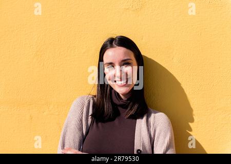 Eine lächelnde Frau, die in eine gelbe Wand guckt Stockfoto