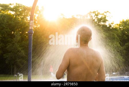 Hannover, Deutschland. 14. Juni 2023. Ein frühmorgendlicher Schwimmer steht unter der Dusche im Licht der aufgehenden Sonne am Annabad Outdoor Pool. Kredit: Julian Stratenschulte/dpa/Alamy Live News Stockfoto