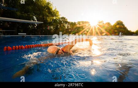 Hannover, Deutschland. 14. Juni 2023. Eine frühmorgendliche Schwimmerin schwimmt im Licht der aufgehenden Sonne am Annabad Outdoor Pool. Kredit: Julian Stratenschulte/dpa/Alamy Live News Stockfoto