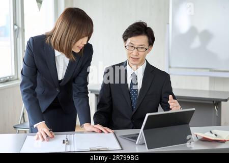Asiatischer Geschäftsmann, der seinen Untergebenen bei seiner Arbeit leitet Stockfoto