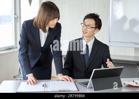 Asiatischer Geschäftsmann, der seinen Untergebenen bei seiner Arbeit leitet Stockfoto