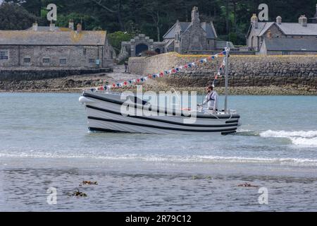 Der Mann fährt ein kleines Motorboot mit roten, weißen und blauen Flöten in Mount's Bay. St. Michael's Mount Harbour Village im Hintergrund. Stockfoto