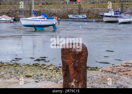 Alte rostige Pfähle am Hafen von St. Michael's Mount mit kleinen Booten und Steinmauer im Hintergrund. Cornwall, England, Großbritannien. Stockfoto