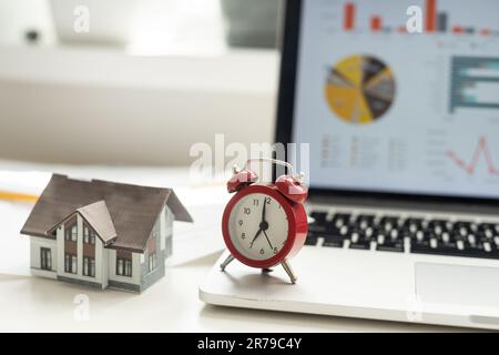 Wecker und Hausmodell. Zeit für eine Hypotheken- oder Immobilienversicherung Stockfoto
