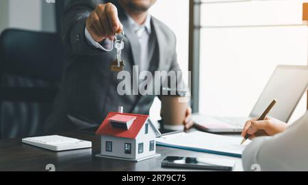 Hausverkaufs- und Hausversicherungskonzept. Immobilienmakler, der Frau Hausschlüssel übergibt und den Kunden bittet, die Dokumente zu unterzeichnen, um den Vertrag rechtmäßig zu machen Stockfoto