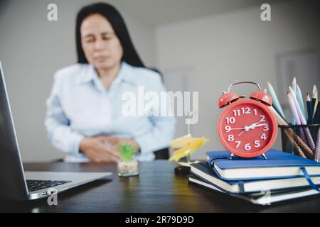 Junge asiatische Geschäftsfrau, die bei der Arbeit sitzt und Stressschmerzen im Magen hat. Concept-Office-Syndrom Bauchschmerzen von Berufskrankheiten, Stockfoto