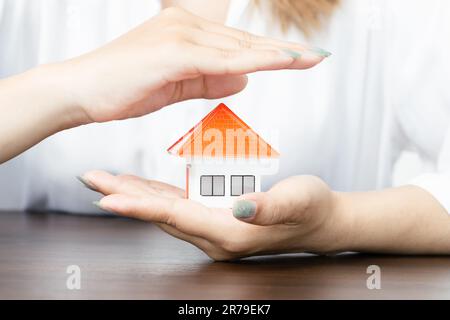 Die Hände einer Frau umgeben ein Hausmodell. Immobilien-, Versicherungs- und Immobilienkonzepte Stockfoto