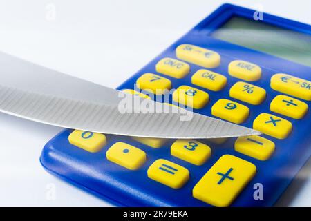 Messerklinge auf Euro-Münze gelegt, Taschenrechner. Konzeptkürzungen, Geldgeschäfte, Verbrechen. Makro. Stockfoto