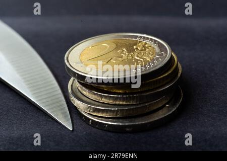 Messerklinge auf Euro-Münze gelegt, Taschenrechner. Konzeptkürzungen, Geldgeschäfte, Verbrechen. Makro. Stockfoto