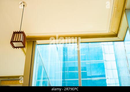 Ruhige, ästhetische Pendelleuchte vor großen Glasfenstern in einem hohen Gebäude. Fesselnde Mischung aus gelber und blauer Atmosphäre Stockfoto