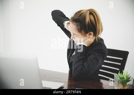 Eine junge asiatische Frau sitzt bei der Arbeit und hat Schmerzen im Nacken, während sie im Büro sitzt Stockfoto