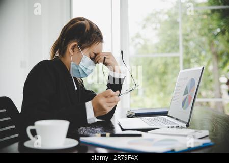 Eine junge asiatische Geschäftsfrau, die am Computer arbeitet, hat Kopfschmerzen, Stress und ist krank von der Arbeit. Krankheitssyndrom in der Praxis. Stockfoto