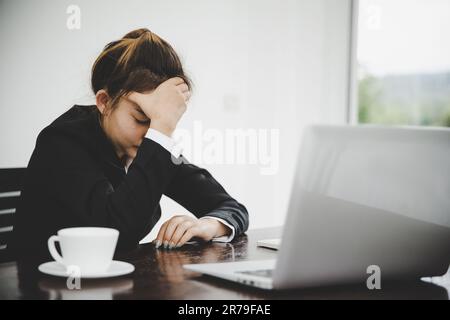 Eine junge asiatische Geschäftsfrau, die am Computer arbeitet, hat Kopfschmerzen, Stress und ist krank von der Arbeit. Krankheitssyndrom in der Praxis. Stockfoto