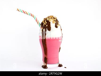 Erdbeermilchshake, Sahne, Mandelstücke und Schokolade, die auf weißem Hintergrund aus dem Glas verschüttet werden Stockfoto