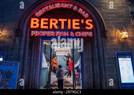 Edinburgh, Schottland, Bertie's richtiges Fish and Chips Restaurant und Bar bei Nacht mit asiatischen Touristen, die sich vor einem Bild am Eingang auf V posieren Stockfoto