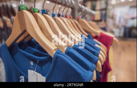 Blaues ärmelloses Hemd auf Holzbügel, das im Bekleidungsgeschäft zum Verkauf an einem Regal hängt. Modegeschäft im Einkaufszentrum. Kleidung an Kleiderbügeln Stockfoto