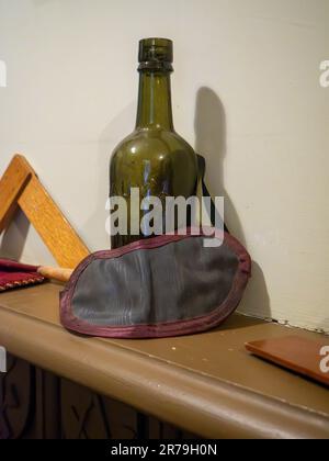 Eine grüne Glasflasche mit einer Augenmaske, die in der Freimaurerhalle im Beamish Museum, Stanley, County Durham, Großbritannien, auf einem Kaminsims hinterlegt wurde Stockfoto