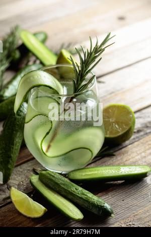 Gin Tonic mit Eis, Rosmarin, Limette und Gurkenscheiben in Milchglas. Cocktail mit Zutaten auf einem alten Holztisch. Stockfoto