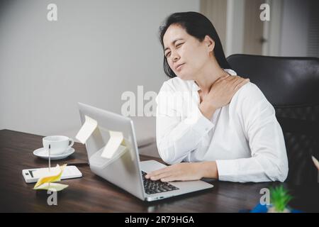 Junge Asiatin sitzt auf der Arbeit und hat Spannungsschmerzen im Nacken. Concept-Office-Syndrom Rückenschmerzen von Berufskrankheiten, weiblich haben Stockfoto