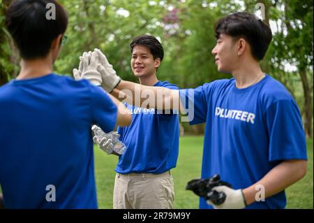 Eine Gruppe fröhlicher junger asiatischer Freiwilliger Hand an Hand oder gibt High Fives, um sich gegenseitig aufzuheitern und sich auf die Arbeit als Freiwillige vorzubereiten. Stockfoto