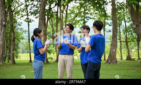 Eine Gruppe fröhlicher junger asiatischer Freiwilliger klatschte in die Hände, um ihre erfolgreiche Wohltätigkeitsveranstaltung im Park zu feiern. CSR-Projekt, Support-Community, Zeichen Stockfoto