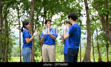 Eine Gruppe fröhlicher junger asiatischer Freiwilliger klatschte in die Hände, um ihre erfolgreiche Wohltätigkeitsveranstaltung im Park zu feiern. Stockfoto