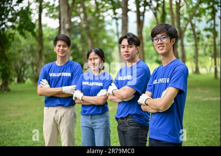 Eine Gruppe glücklicher, junger asiatischer Freiwilliger in Uniform, die im öffentlichen Park mit verschränkten Armen standen und in die Kamera blickten. Freiwilligenarbeit, toge Stockfoto