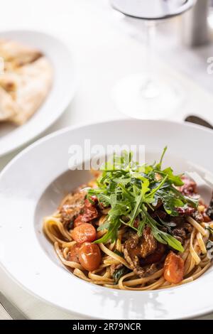 Tomatenlinguine mit Fleisch und Rucola auf einem schicken Teller. Stockfoto