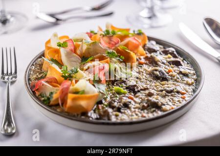 Italienisches Pilzrisotto mit Wurzelgemüse und Petersilie, serviert auf einem Teller auf einem Restauranttisch. Stockfoto