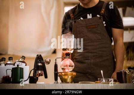 Professionelle Kaffeemaschine – Barista, der einen Kaffeesauger verwendet, um heißen Espresso im Café zuzubereiten. Alternativer Siphon-Aufbrühvorgang. Start-Up-Unternehmen Stockfoto