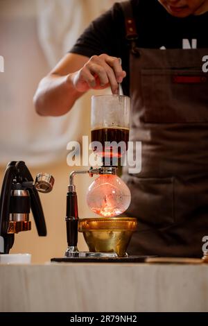 Professionelle Kaffeemaschine – Barista, der einen Kaffeesauger verwendet, um heißen Espresso im Café zuzubereiten. Alternativer Siphon-Aufbrühvorgang. Start-Up-Unternehmen Stockfoto