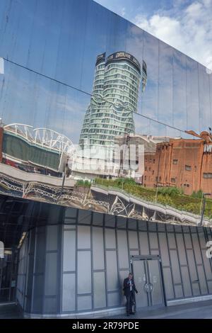 Birmingham, Großbritannien. Vor dem Bahnhof New Street mit seiner Spiegelfassade wartet ein Passagier unter einer Reflexion des Rotunda-Gebäudes Stockfoto