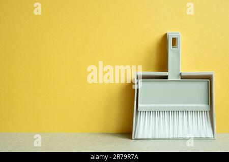 Grauer Besen und Kehrschaufel auf grauen Tisch. Gelber Hintergrund. Reinigungskonzept Hausarbeit. Speicherplatz kopieren Stockfoto